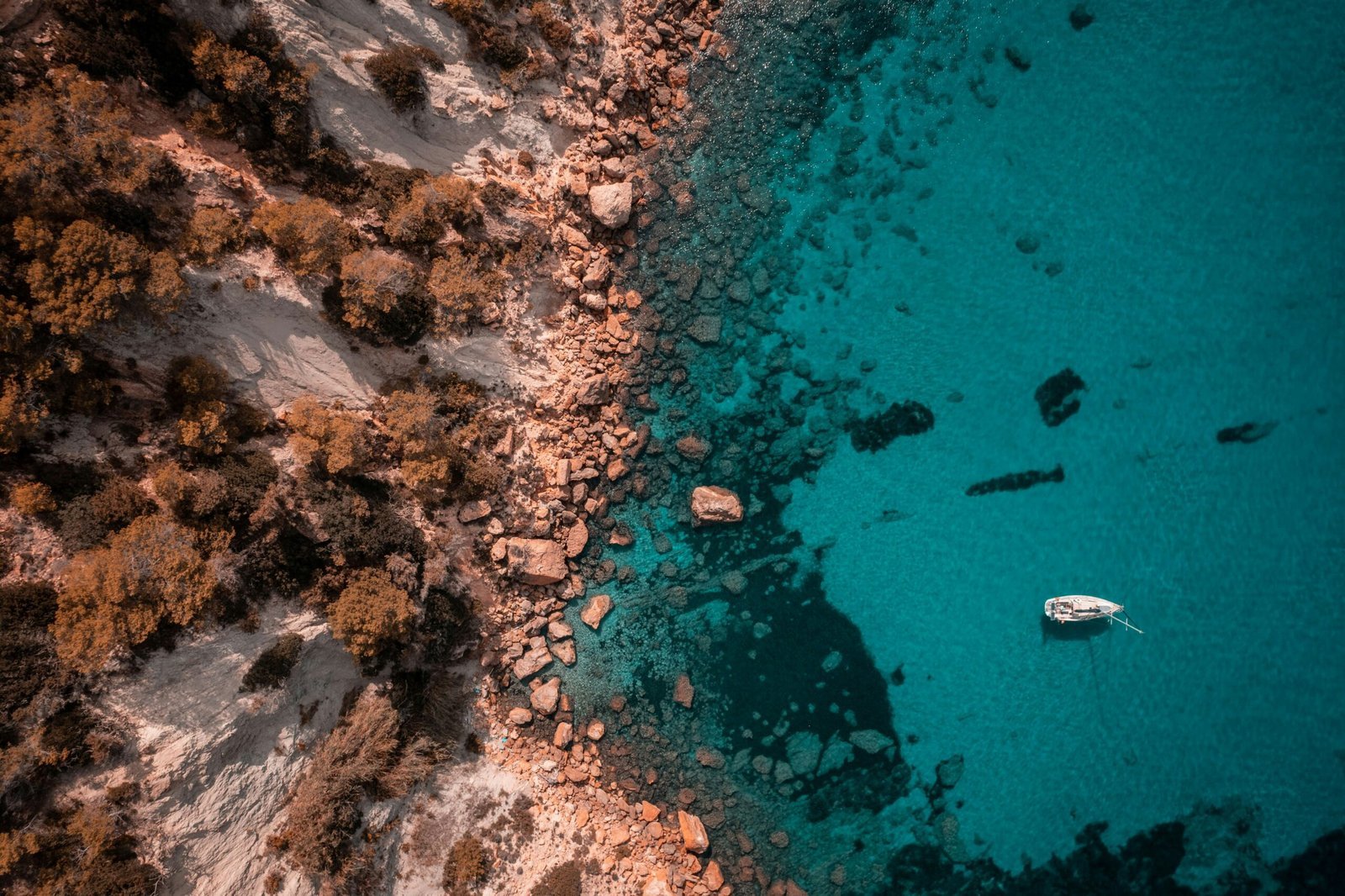 Aerial view of rocky coast, clear blue water, and boat - MaherTech Inc (saas platform)